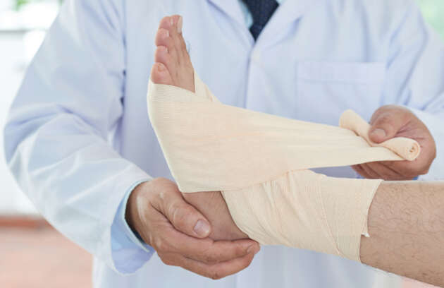 Imagem mostrando o médico enfaixando o pé de uma paciente que teve um problema ortopédico